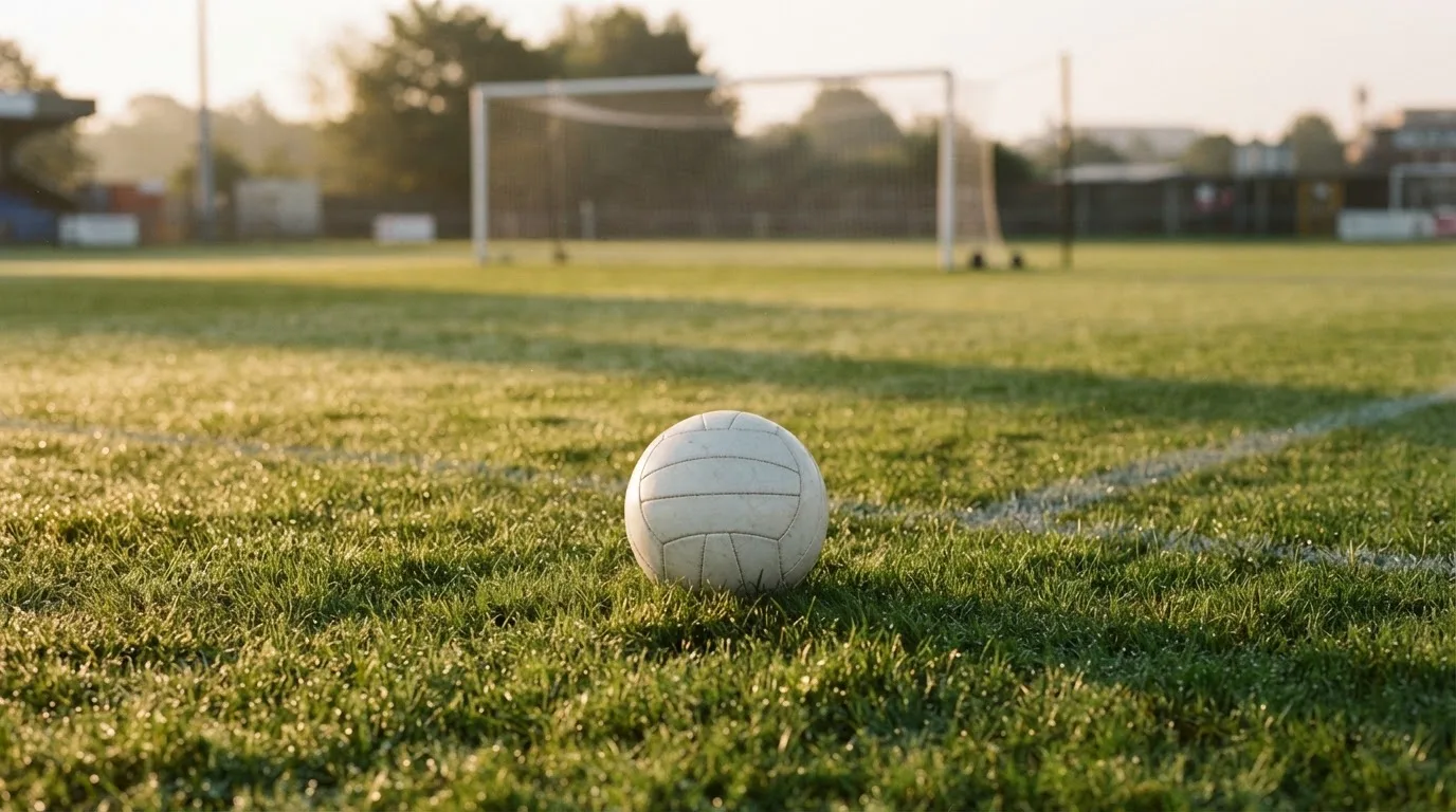 Ein Fußball auf dem Rasen vor einem leeren Tor im frühen Morgenlicht.