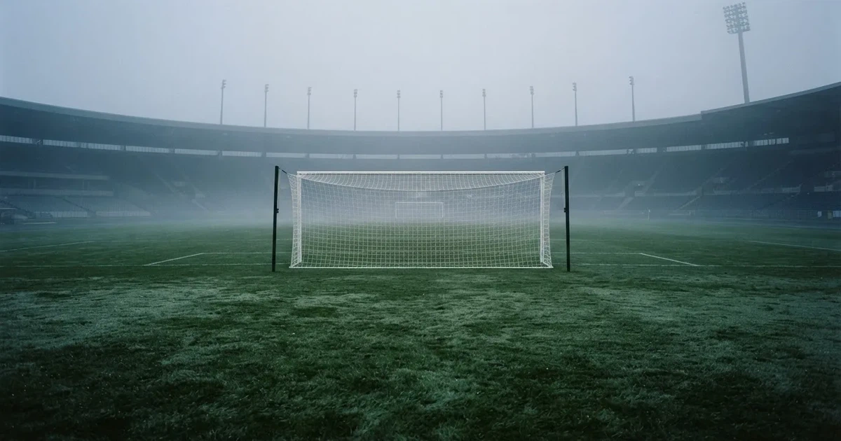 Ein Fußballtor mit Netz steht auf einem leeren Platz im Nebel der Morgendämmerung, der Rasen ist taufeucht.
