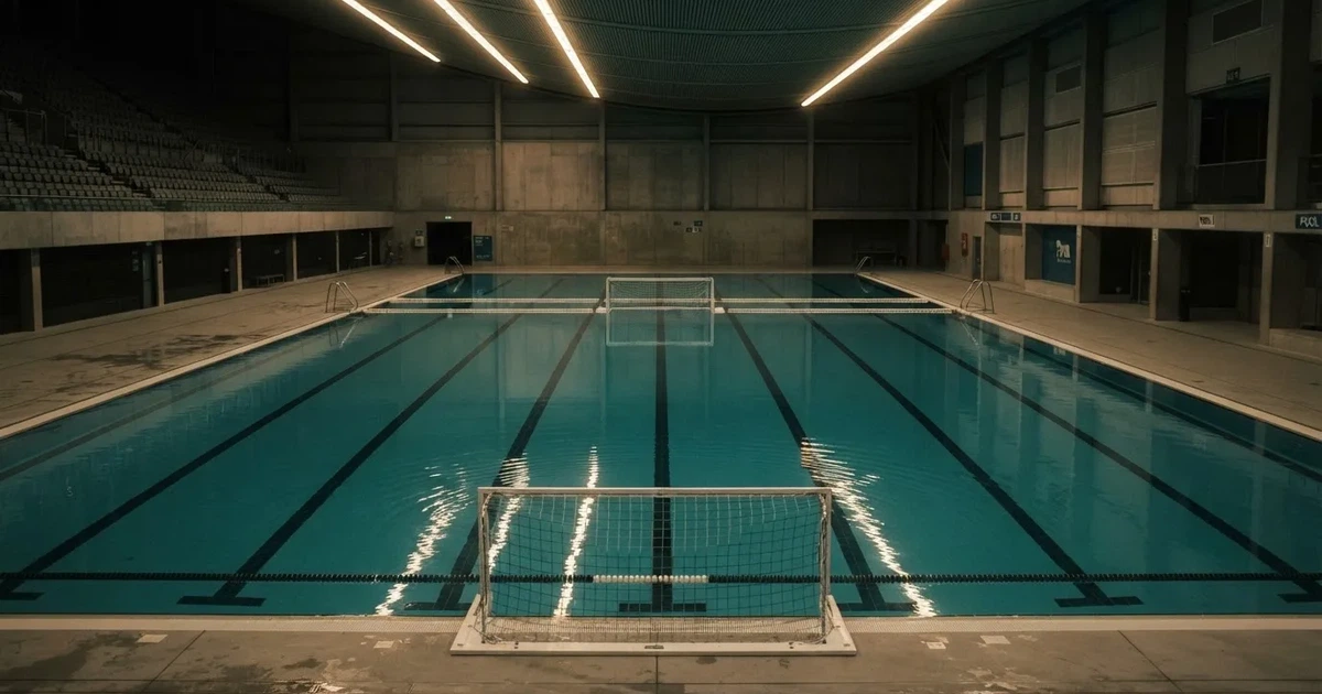 Ein Schwimmbecken mit türkisfarbenem Wasser und zwei schwimmenden Torrahmen am gegenüberliegenden Beckenrand, menschenleer unter Hallenlicht.